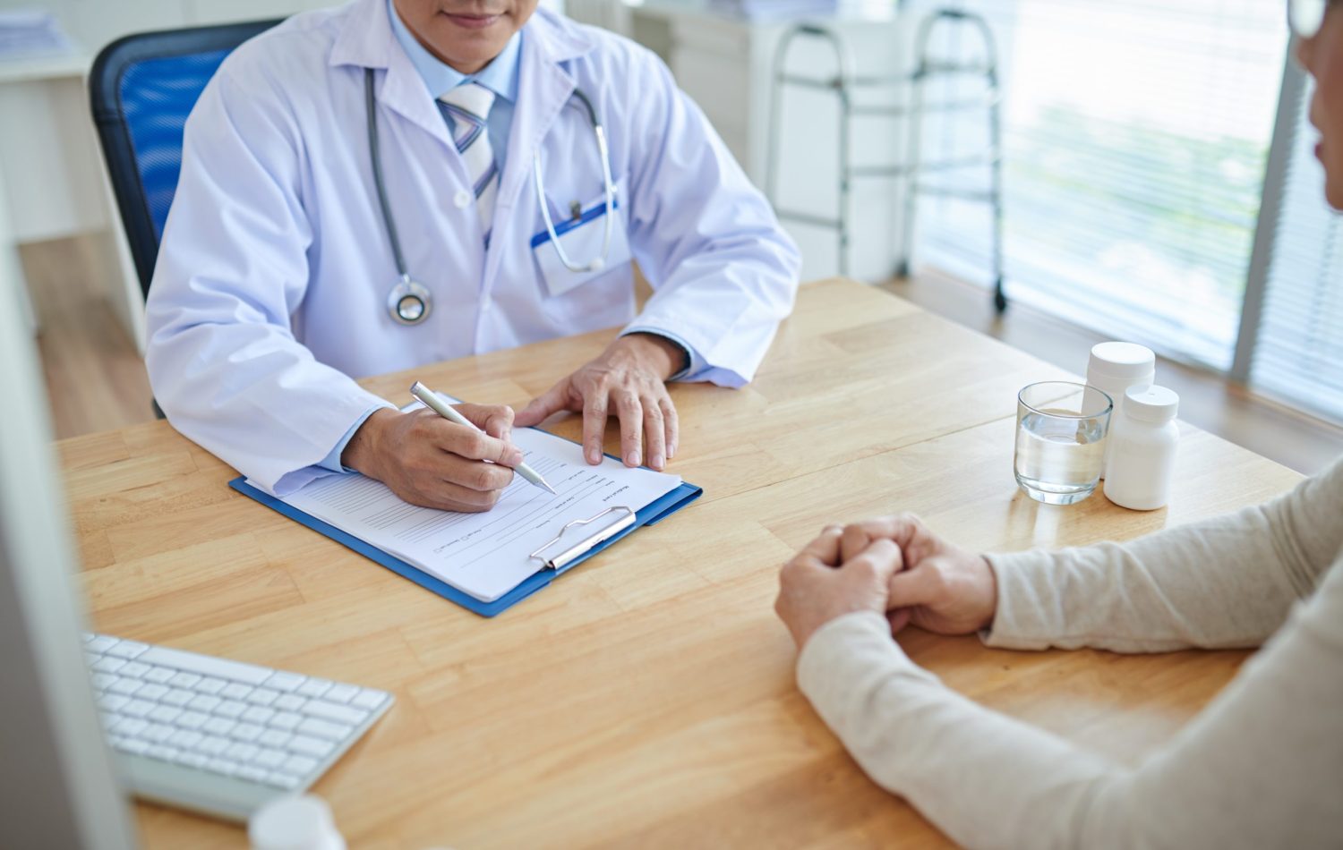 close-up shot of a male doctor filling in a medical record of a patient sitting opposite to him