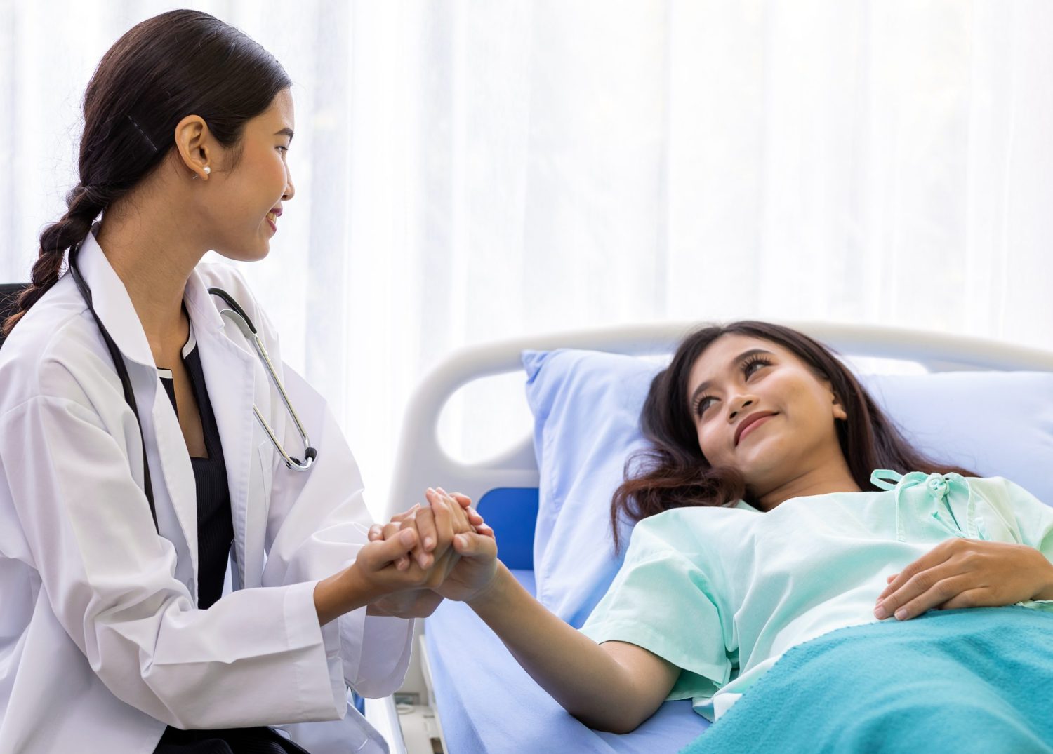 a female doctor holding the hand of a female patient lying in bed